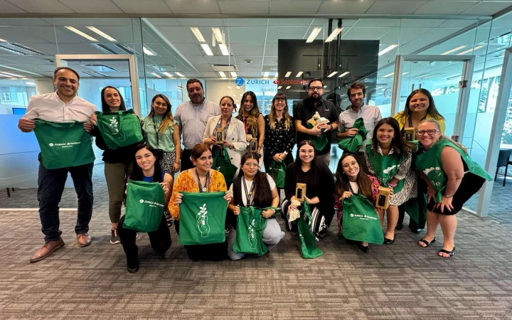 Grupo de colaboradores de Zurich Santander Chile posando en la oficina tras la intervención de reciclaje, sosteniendo bolsas ecológicas verdes y reconocimientos de participación.