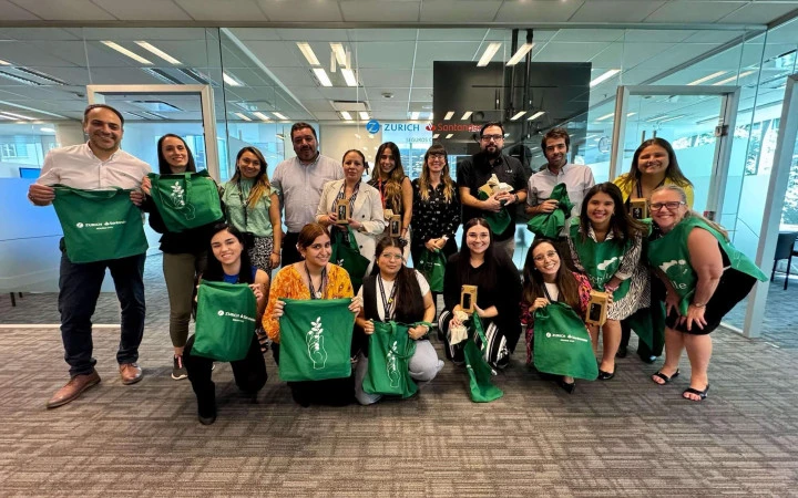 Grupo de colaboradores de Zurich Santander Chile posando en la oficina tras la intervención de reciclaje, sosteniendo bolsas ecológicas verdes y reconocimientos de participación.